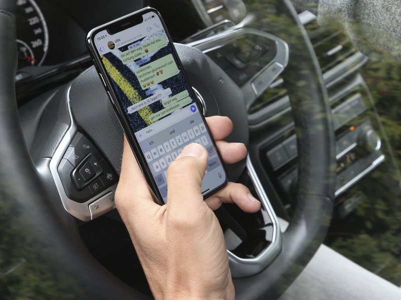Ablenkung am Steuer durch Smartphone-Nutzung Person schreibt während der Fahrt eine WhatsApp-Nachricht am Steuer eines Autos